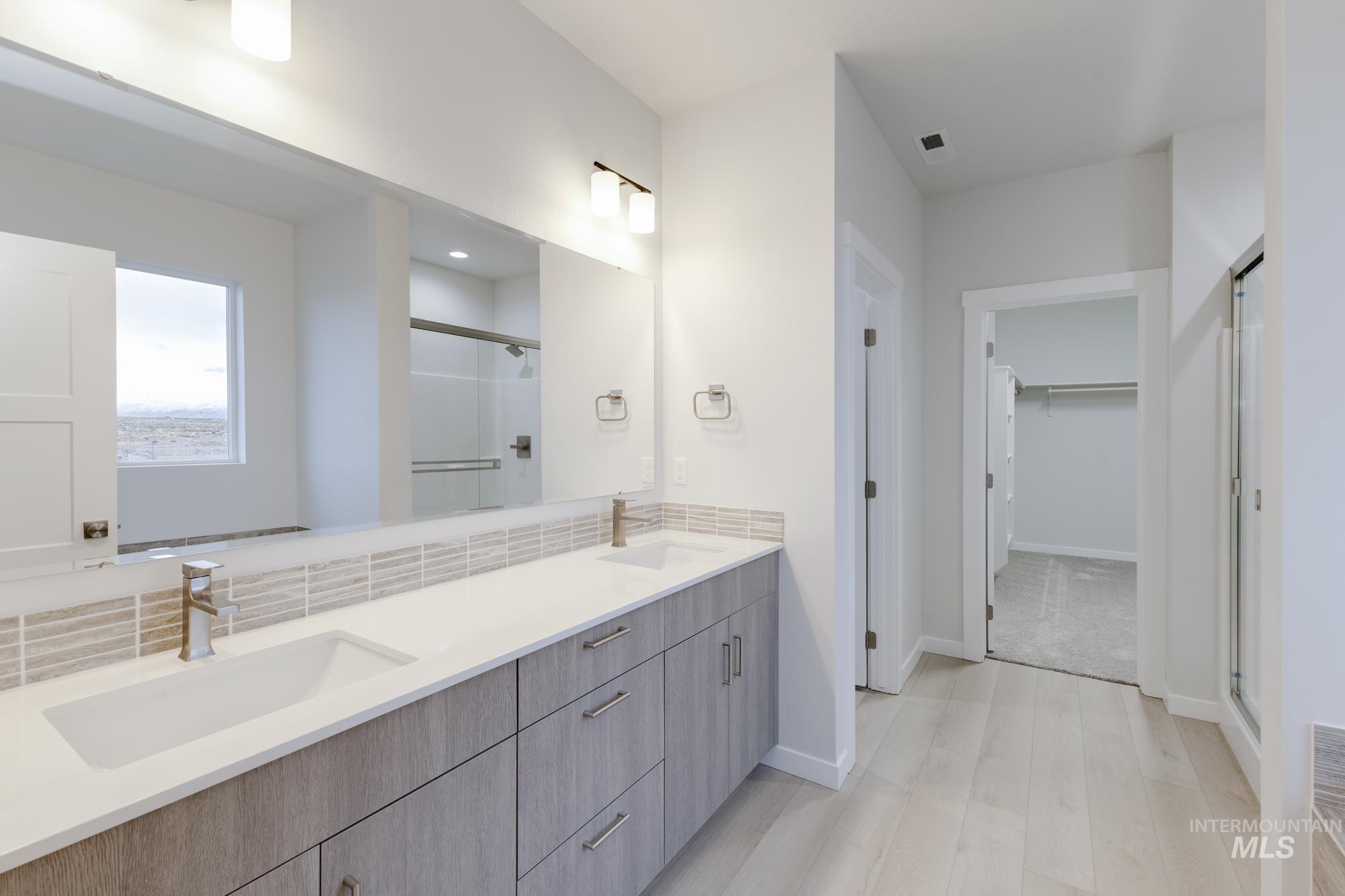 Bathroom with a stall shower, a spacious closet, double vanity, light wood finished floors, and backsplash