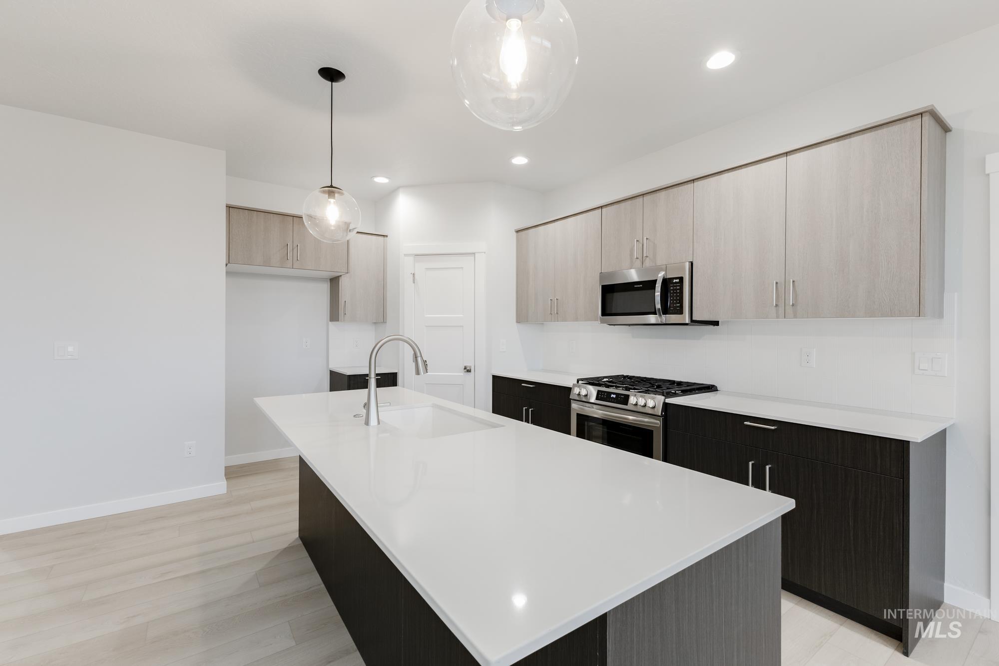 Kitchen featuring modern cabinets, decorative light fixtures, appliances with stainless steel finishes, a center island with sink, and light stone counters