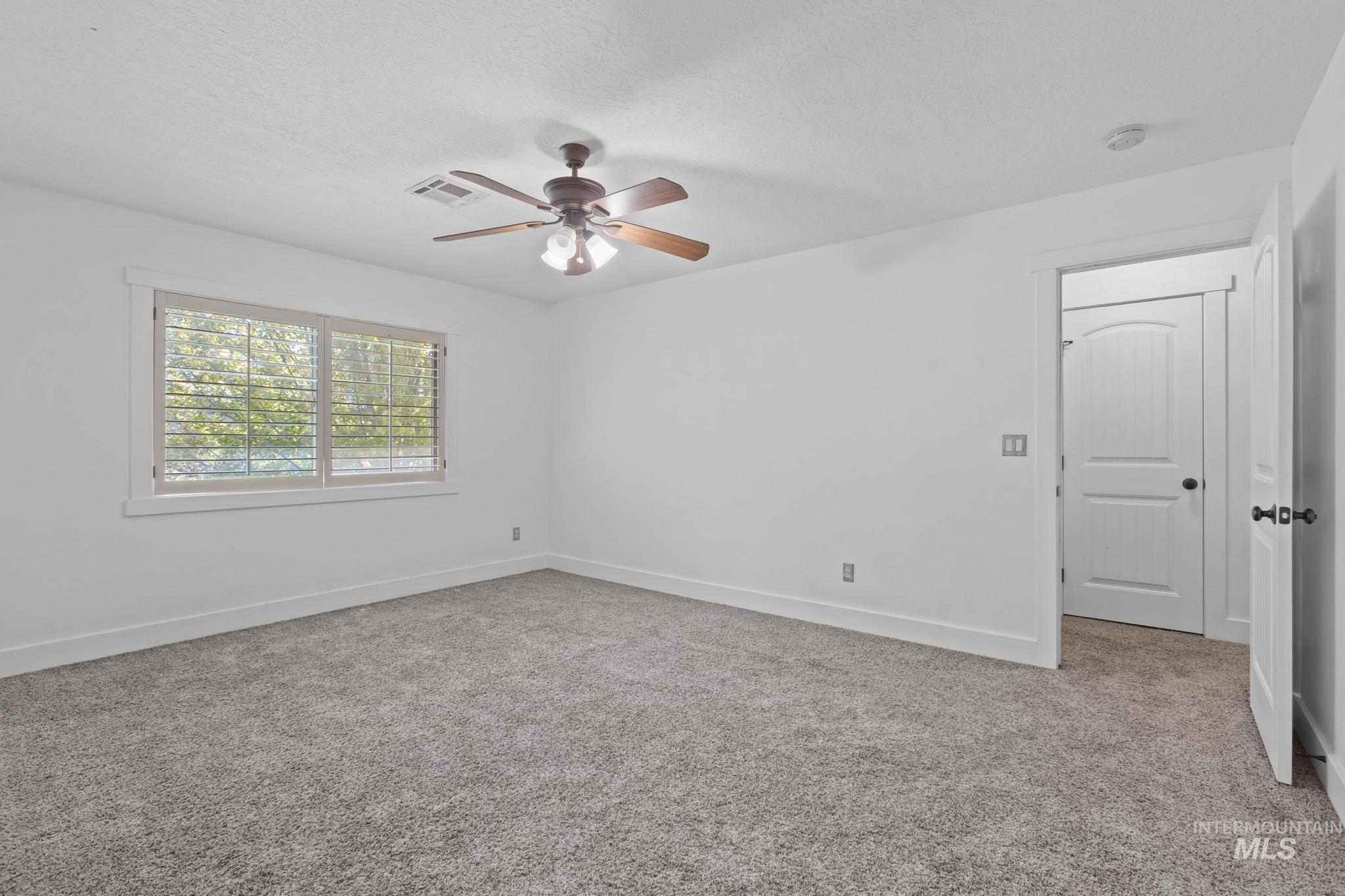 Spare room featuring light colored carpet, a textured ceiling, and ceiling fan