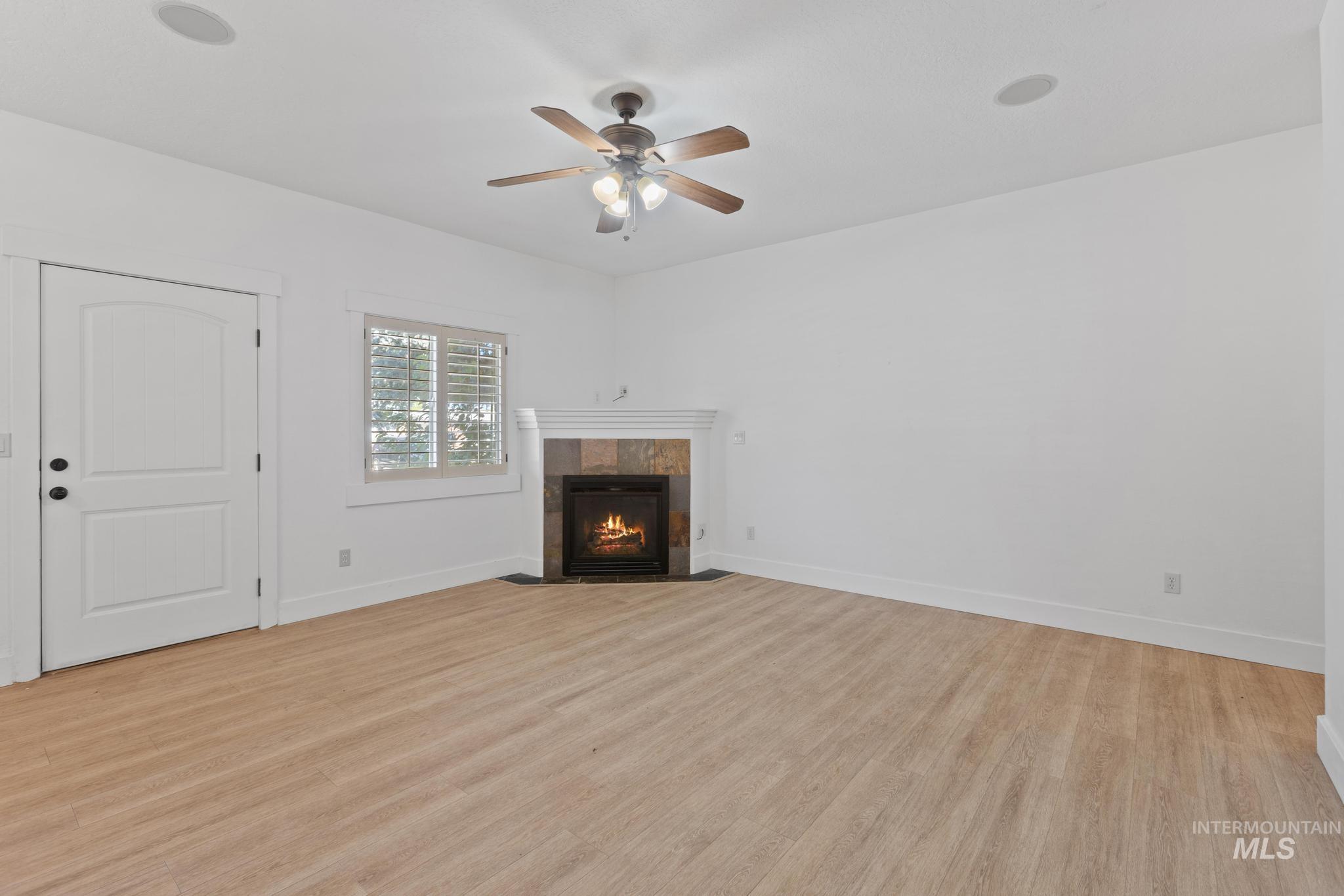 Unfurnished living room featuring a tile fireplace, light wood-style flooring, and a ceiling fan