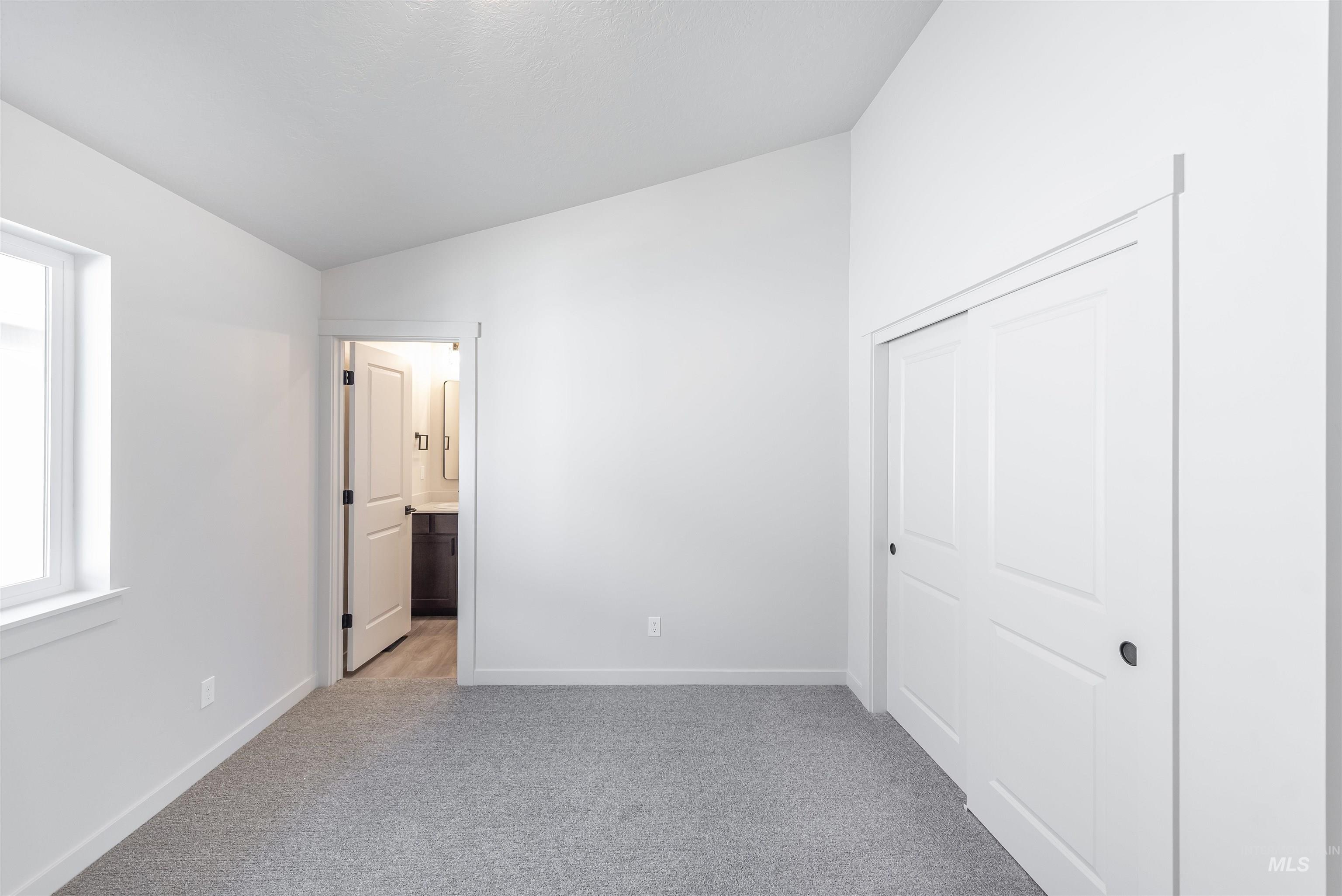 Unfurnished bedroom featuring light colored carpet, vaulted ceiling, ensuite bath, and a closet