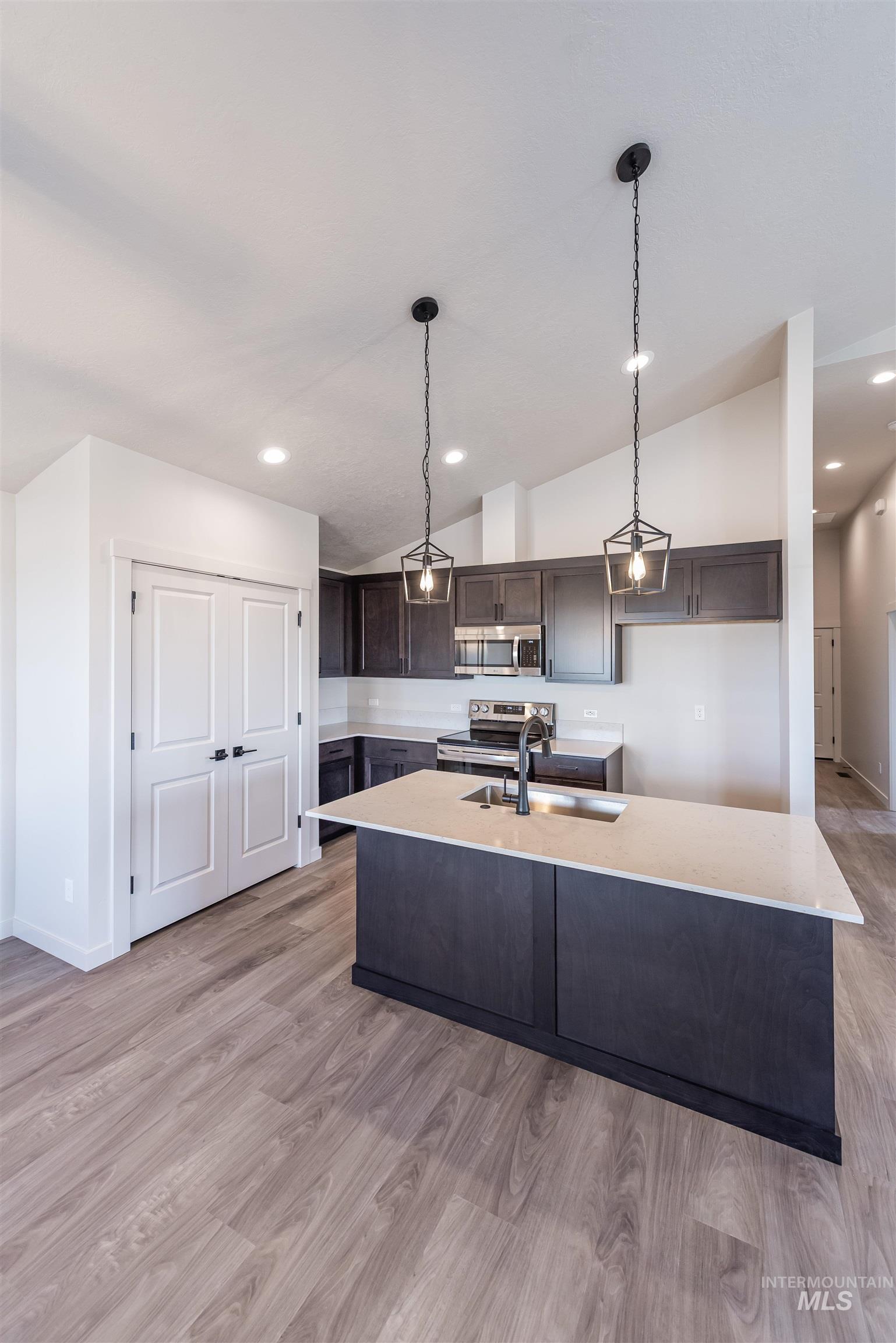 Kitchen with pendant lighting, dark brown cabinetry, light wood-style floors, vaulted ceiling, and recessed lighting