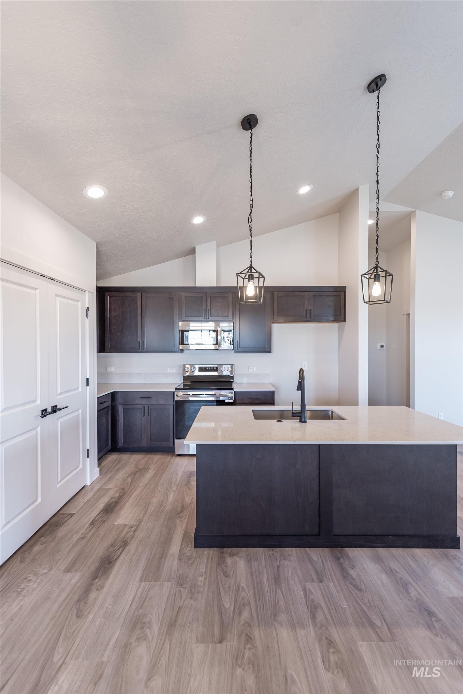 Kitchen featuring dark brown cabinets, stainless steel appliances, light wood finished floors, pendant lighting, and lofted ceiling