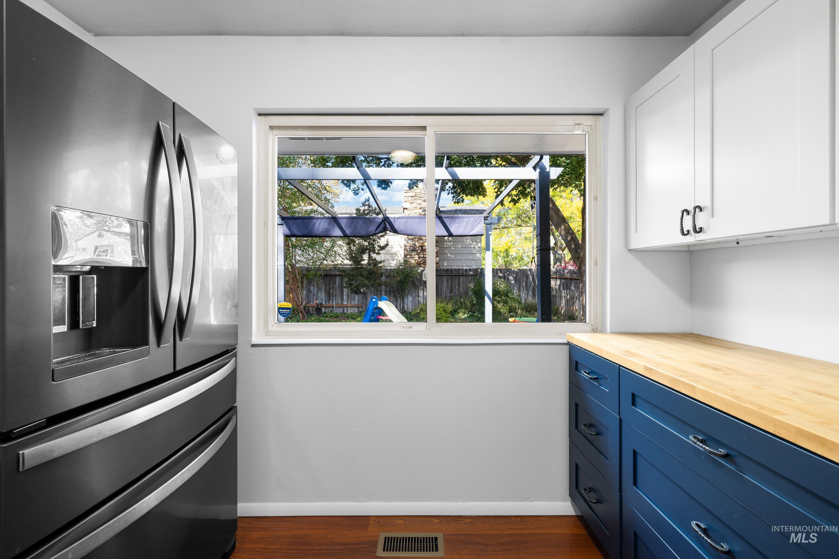 Kitchen featuring stainless steel fridge with ice dispenser, butcher block counters, white cabinetry, blue cabinets, and dark wood-type flooring