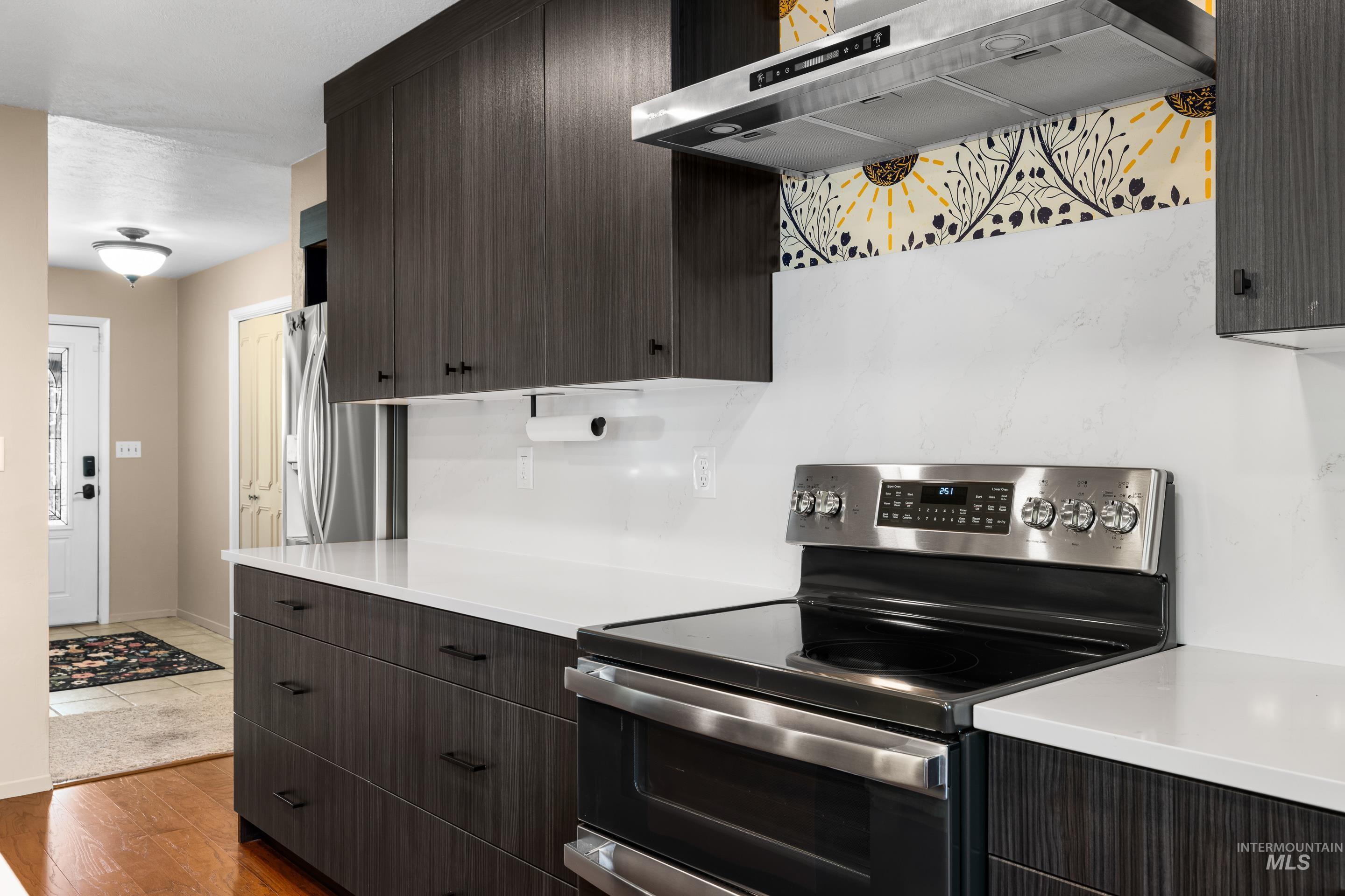 Kitchen featuring stainless steel appliances, ventilation hood, light wood-type flooring, and dark brown cabinetry