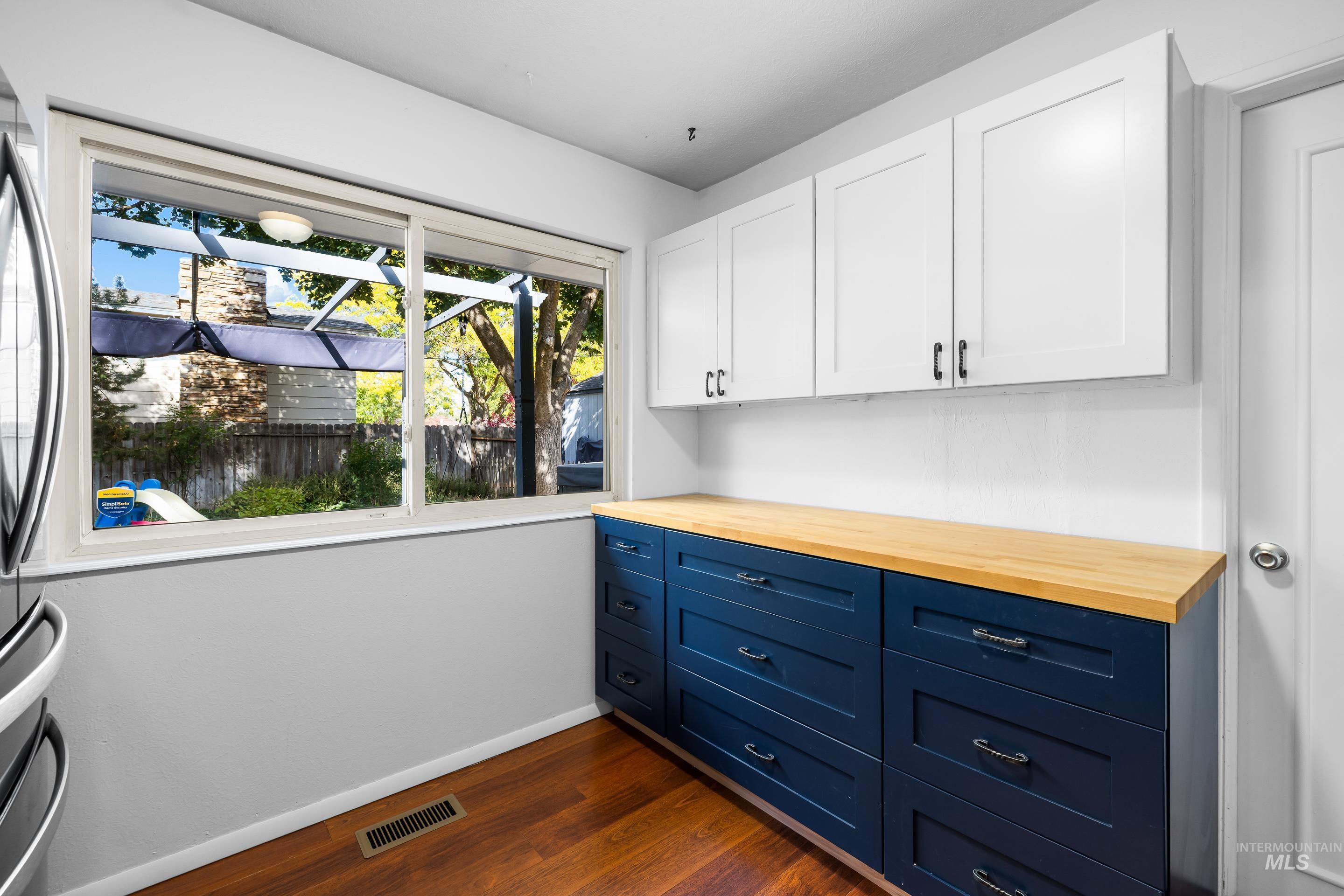 Kitchen with butcher block countertops, blue cabinetry, dark wood finished floors, white cabinetry, and stainless steel fridge