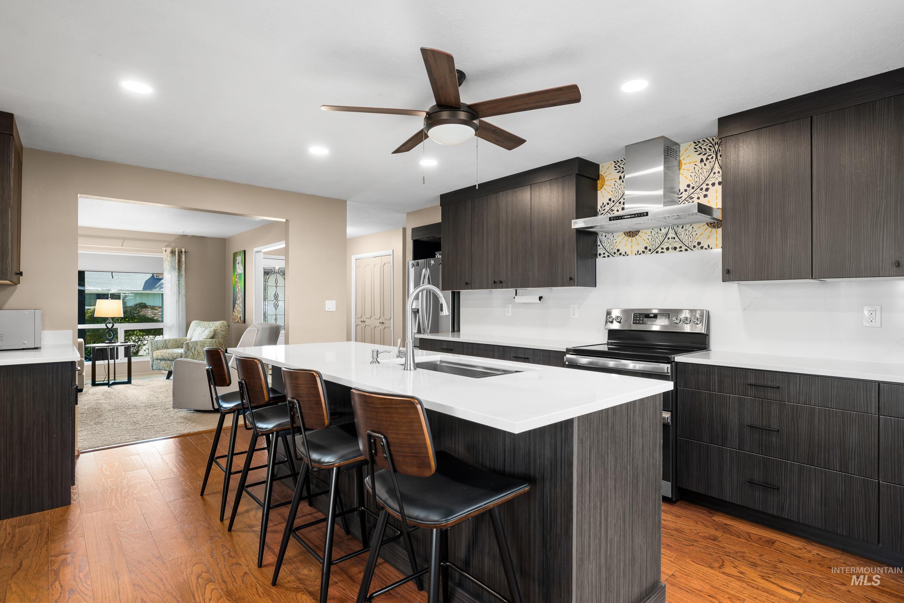 Kitchen with modern cabinets, wall chimney exhaust hood, dark brown cabinetry, light wood-type flooring, and stainless steel range with electric cooktop