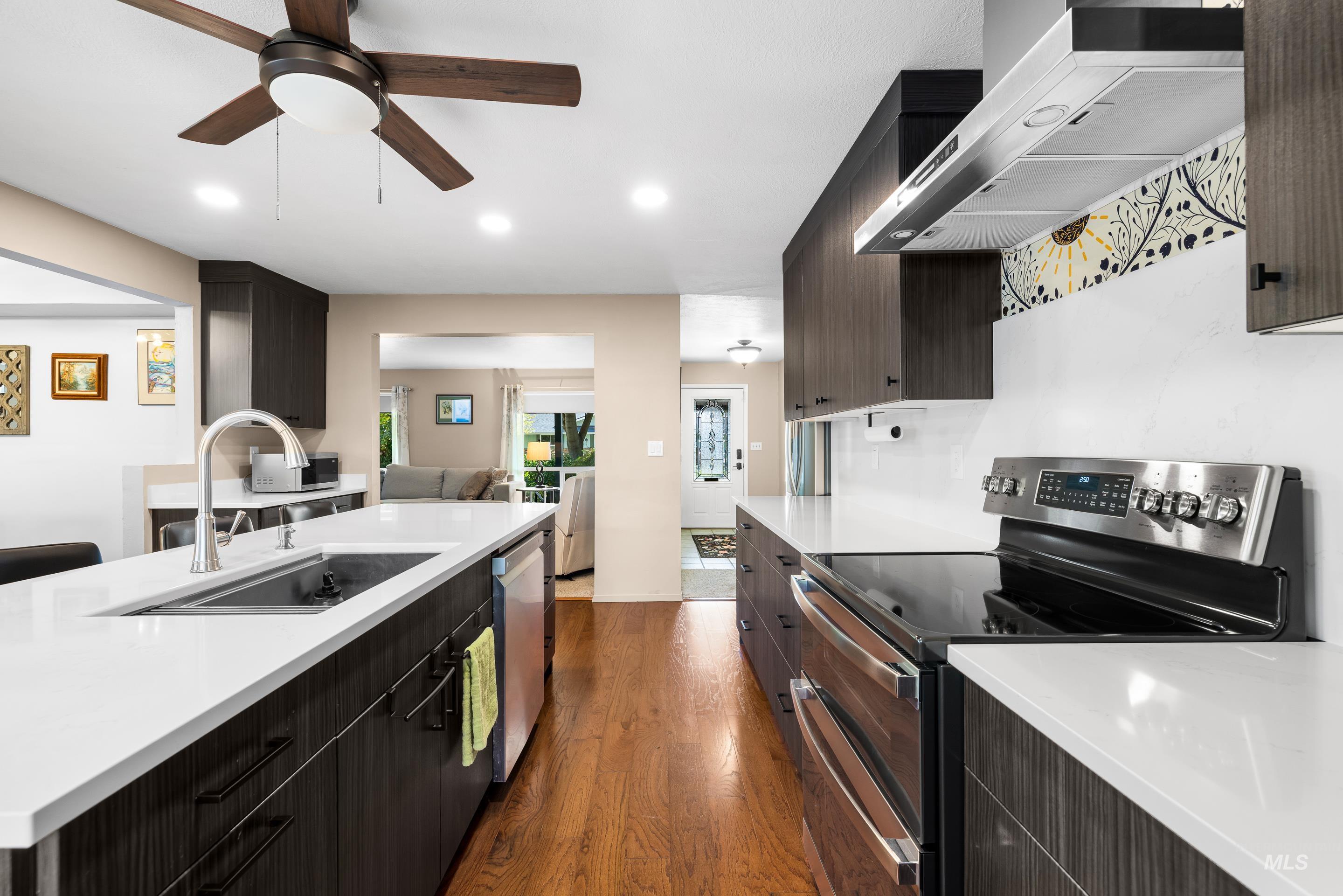 Kitchen with stainless steel appliances, wall chimney exhaust hood, dark wood-type flooring, open floor plan, and modern cabinets