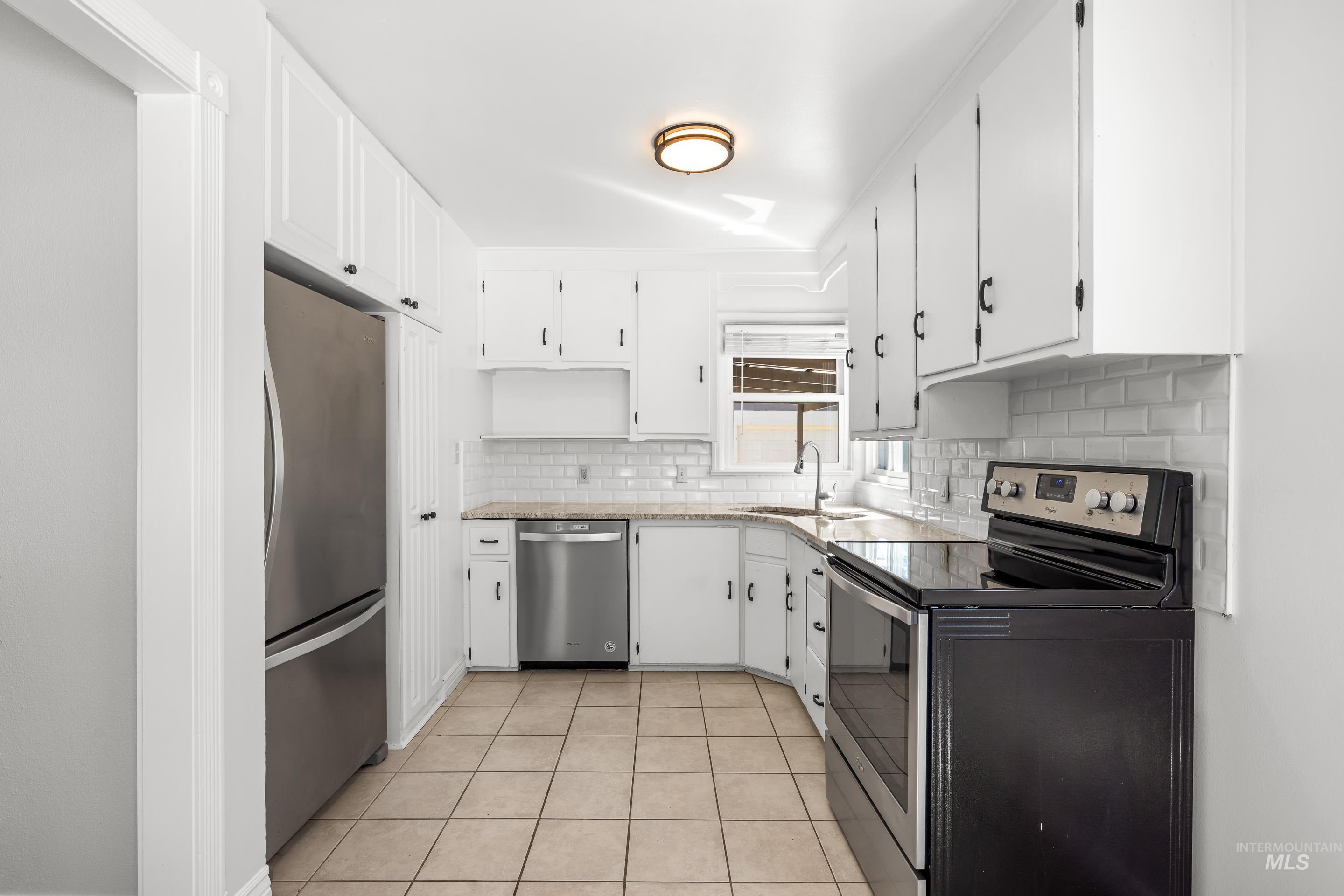 Kitchen with stainless steel appliances, decorative backsplash, light tile patterned floors, and white cabinets