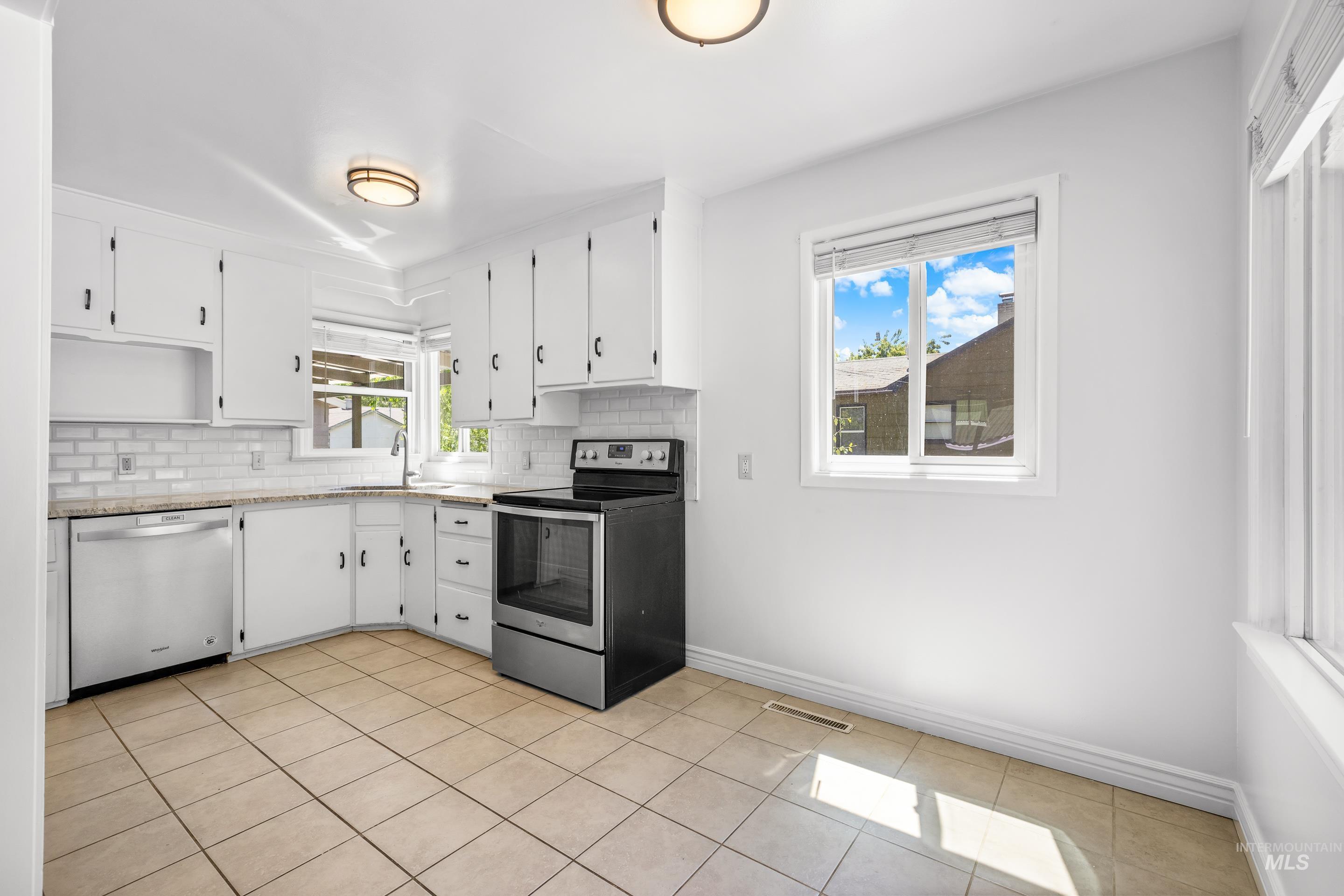Kitchen with stainless steel appliances, backsplash, white cabinets, and light tile patterned floors