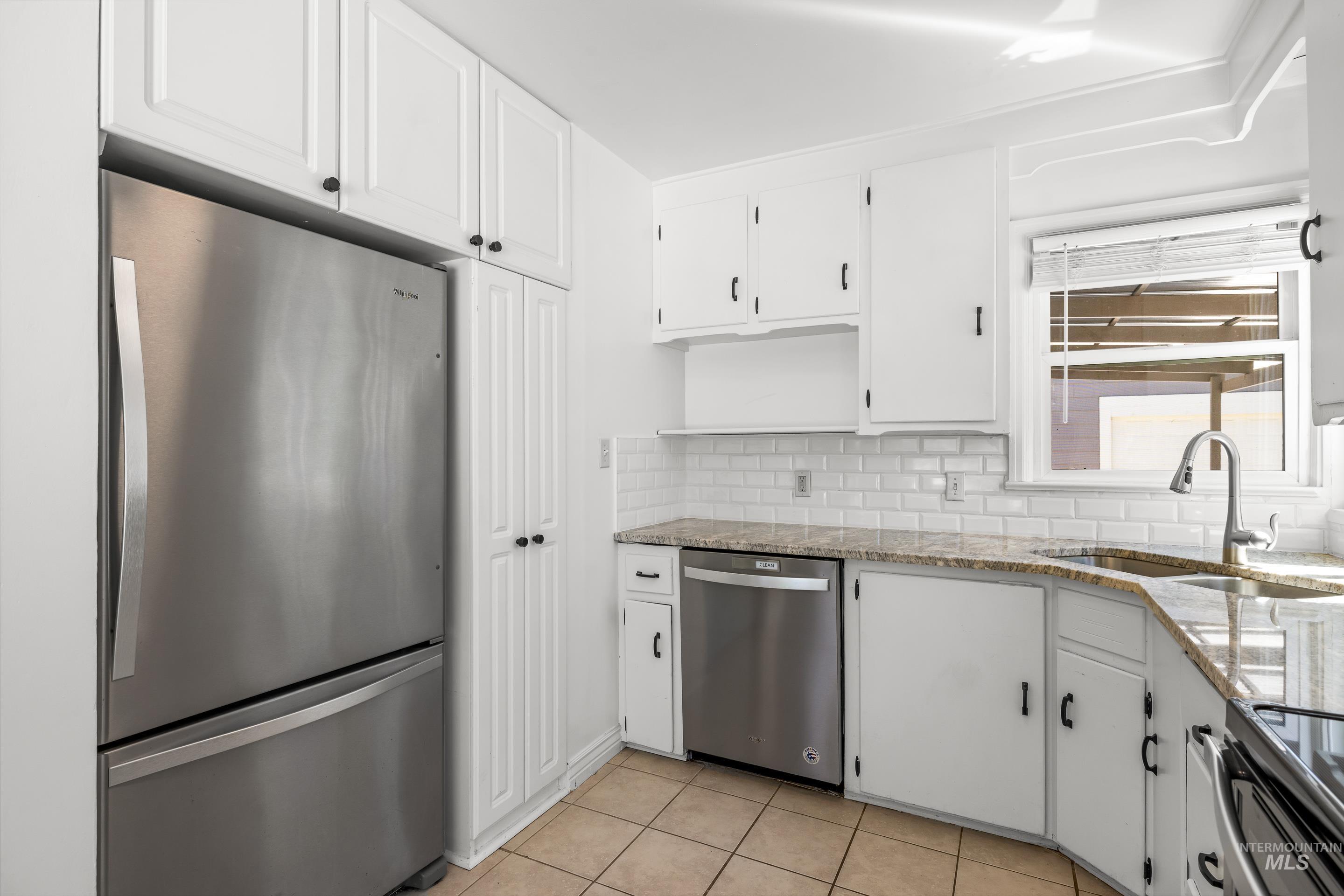 Kitchen featuring stainless steel appliances, white cabinets, light tile patterned floors, light stone countertops, and backsplash