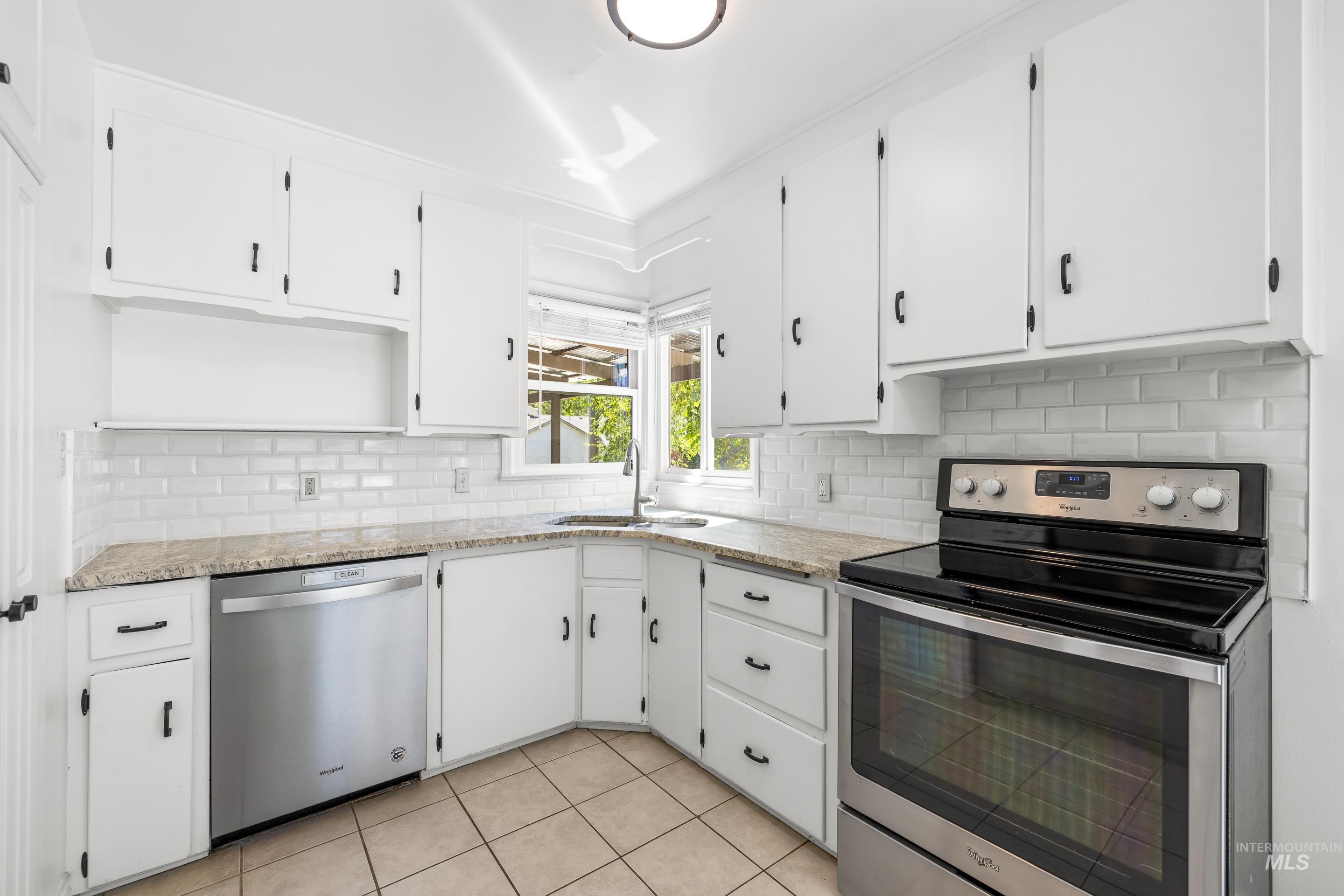 Kitchen featuring stainless steel appliances, white cabinetry, tasteful backsplash, and light stone counters