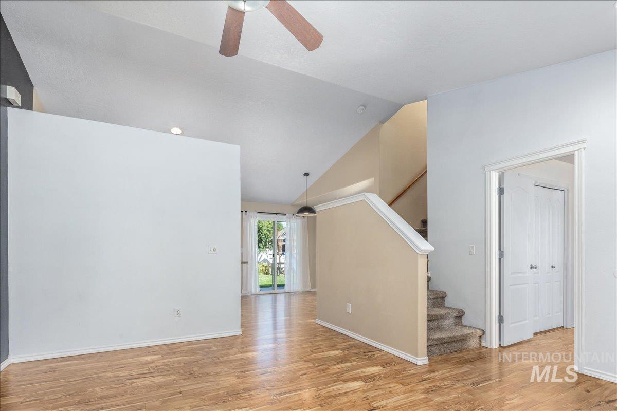 Unfurnished living room featuring stairway, lofted ceiling, light wood-type flooring, and ceiling fan