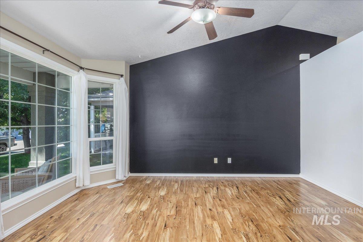 Spare room featuring light wood finished floors, ceiling fan, and vaulted ceiling