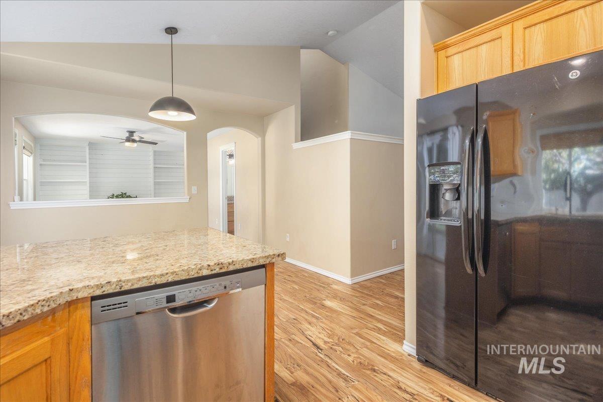 Kitchen featuring black refrigerator with ice dispenser, dishwasher, arched walkways, pendant lighting, and light wood finished floors