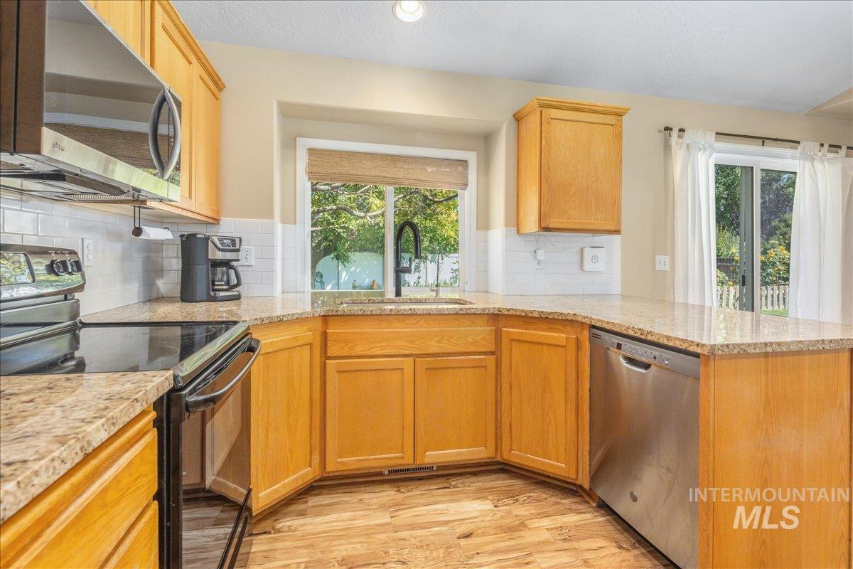Kitchen with stainless steel appliances, light wood-style flooring, plenty of natural light, decorative backsplash, and a textured ceiling