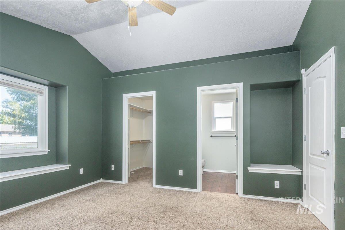 Unfurnished bedroom with carpet floors, connected bathroom, a spacious closet, a textured ceiling, and lofted ceiling