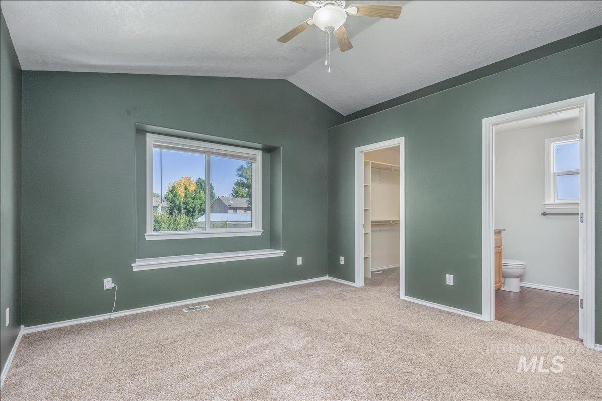 Unfurnished bedroom with multiple windows, vaulted ceiling, carpet floors, a spacious closet, and ensuite bath