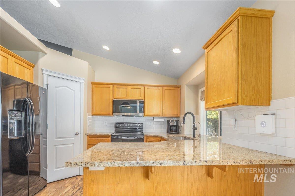 Kitchen featuring black appliances, light stone counters, backsplash, a peninsula, and recessed lighting