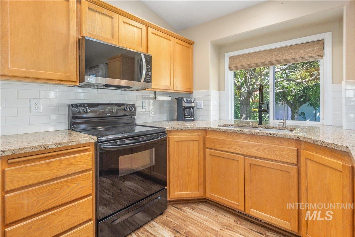Kitchen with black range with electric stovetop, stainless steel microwave, light stone counters, and light wood-style floors