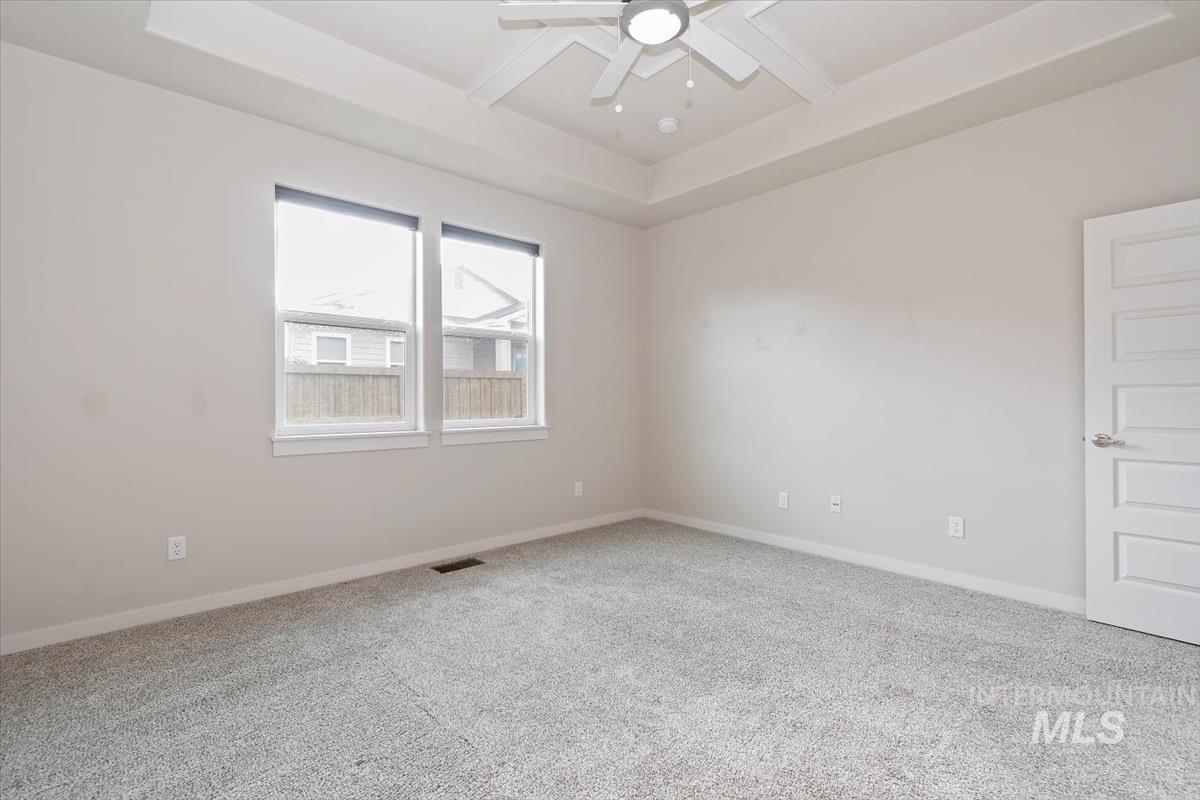 Unfurnished room with a raised ceiling, light carpet, and a ceiling fan