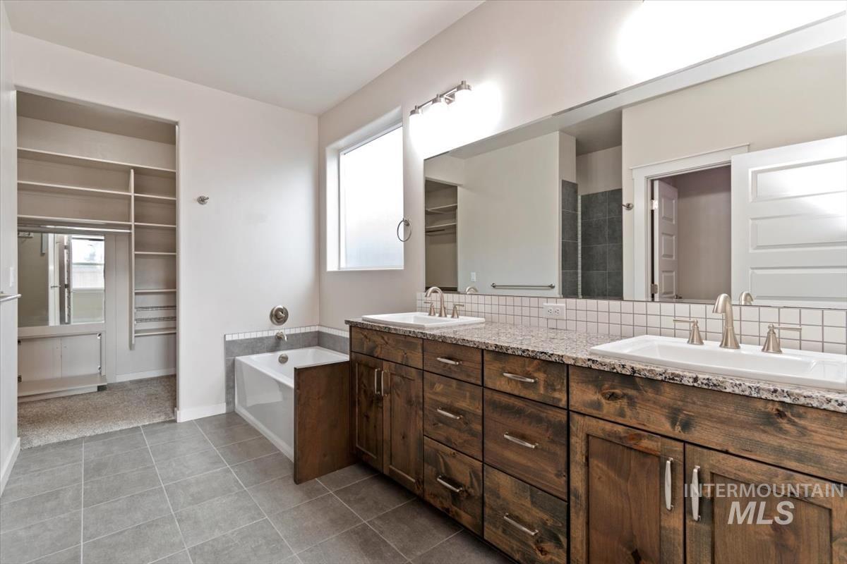 Full bath featuring a spacious closet, double vanity, backsplash, dark tile patterned flooring, and a bath