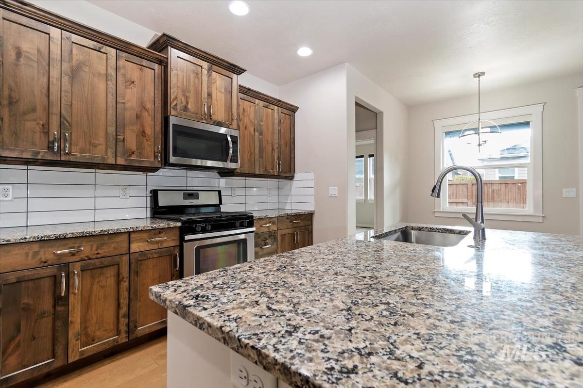 Kitchen featuring appliances with stainless steel finishes, light stone counters, pendant lighting, decorative backsplash, and recessed lighting