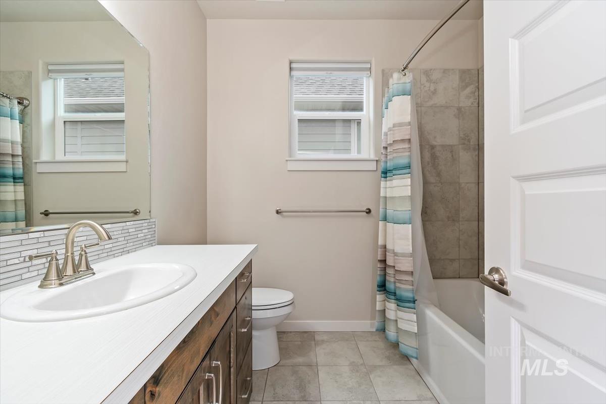 Full bath featuring vanity, shower / tub combo with curtain, light tile patterned flooring, and backsplash