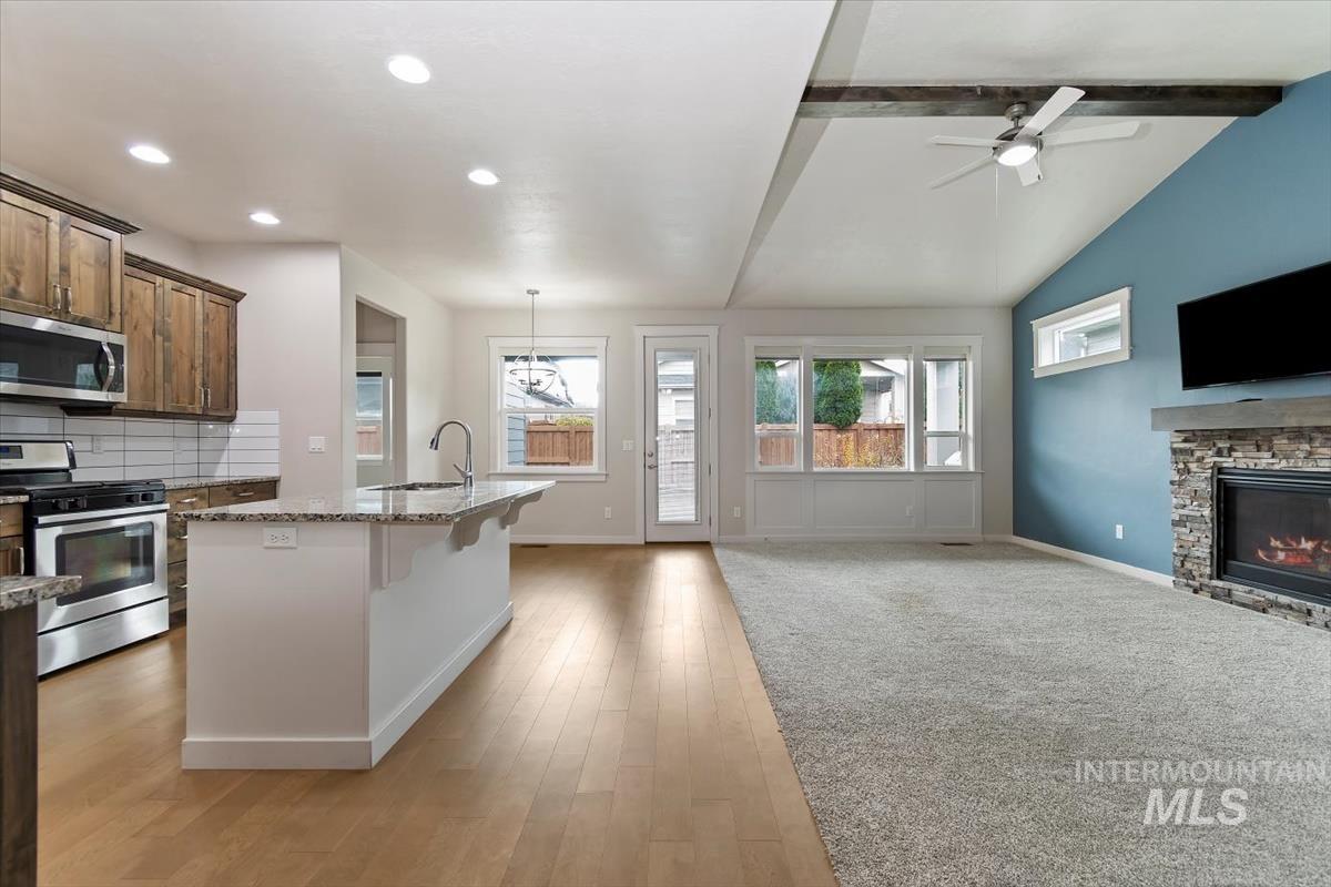 Kitchen with appliances with stainless steel finishes, a breakfast bar area, open floor plan, a ceiling fan, and light stone countertops