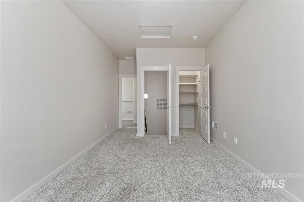 Unfurnished bedroom with a walk in closet, carpet flooring, and attic access