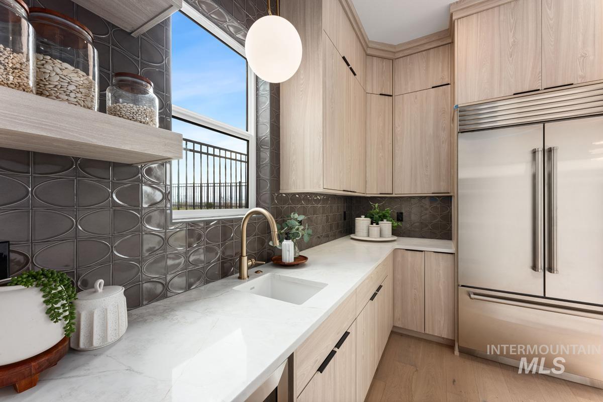 Kitchen with stainless steel built in refrigerator, light wood finish cabinets, light stone countertops, and tasteful backsplash