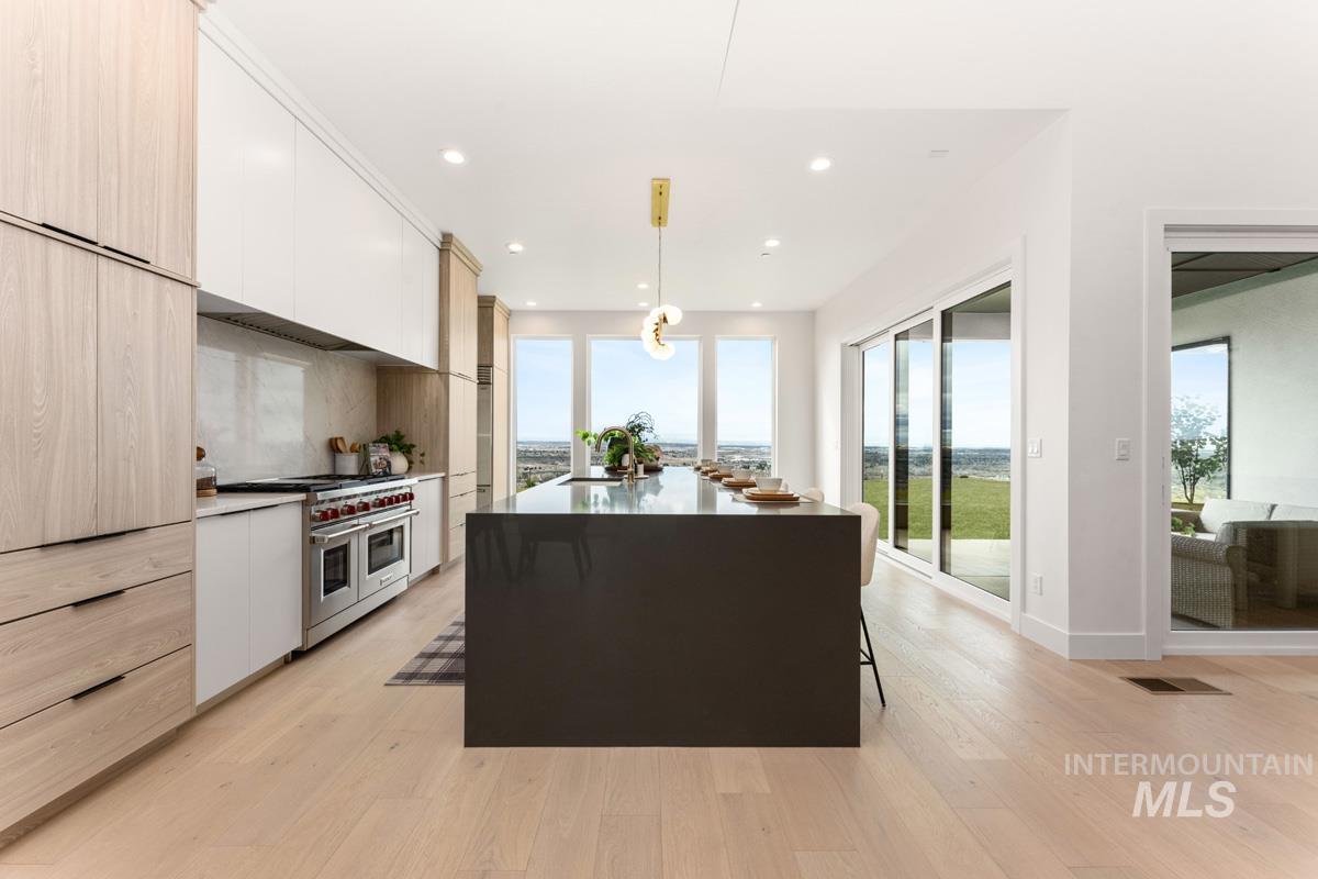 Dual tone kitchen with dual tone cabinets, double oven range, hanging light fixtures, light wood finished floors, and light stone countertops