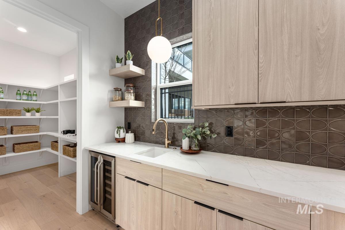 Indoor wet bar with light wood finish cabinets, wine cooler, light wood-style flooring, light stone countertops, and decorative backsplash