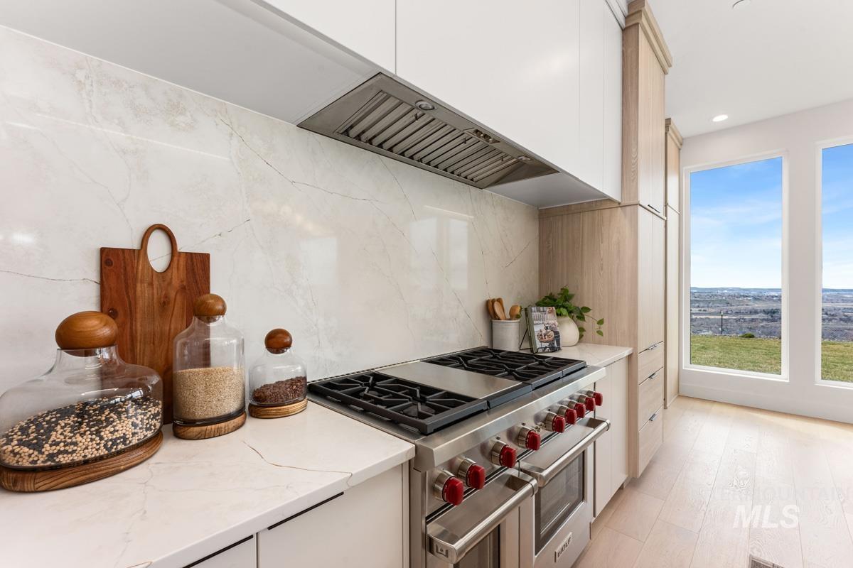 Kitchen with range with two ovens, light stone countertops, exhaust hood, light wood-style floors, and decorative backsplash