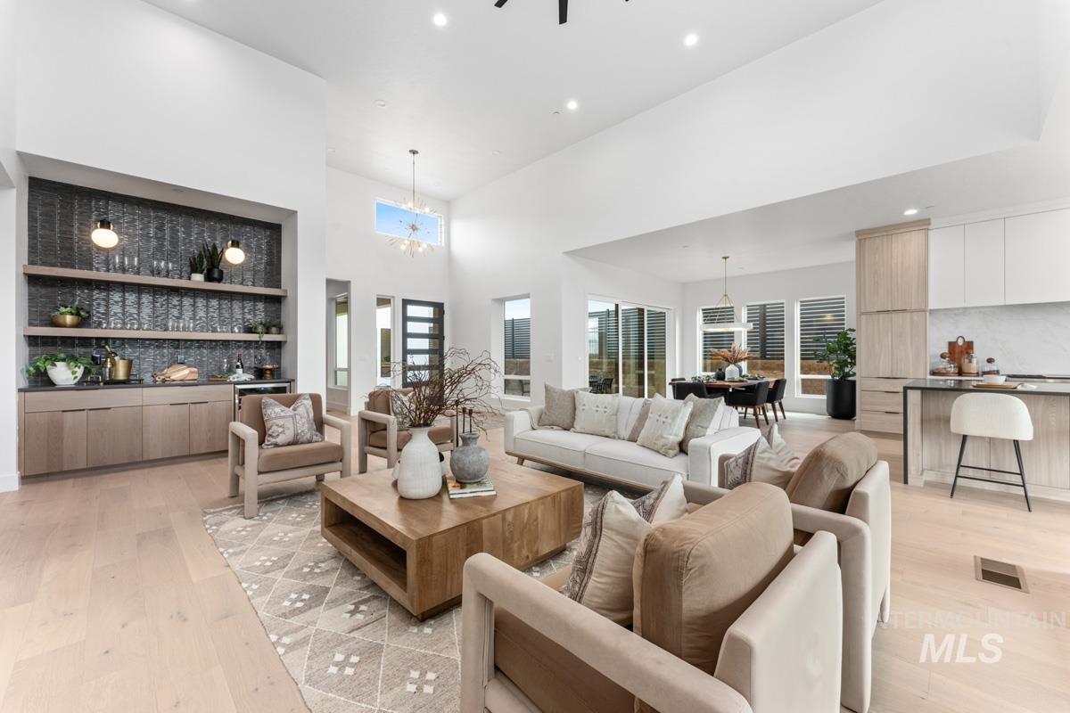 Living room featuring bar with sink, light wood finished floors, a high ceiling, suspended lighting, and built in features