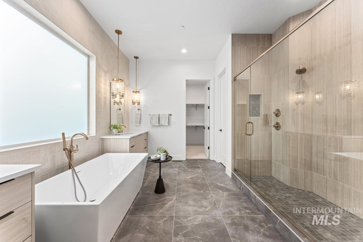 Full bathroom with vanity, a spacious closet, a freestanding bath, a stall shower, and tile walls