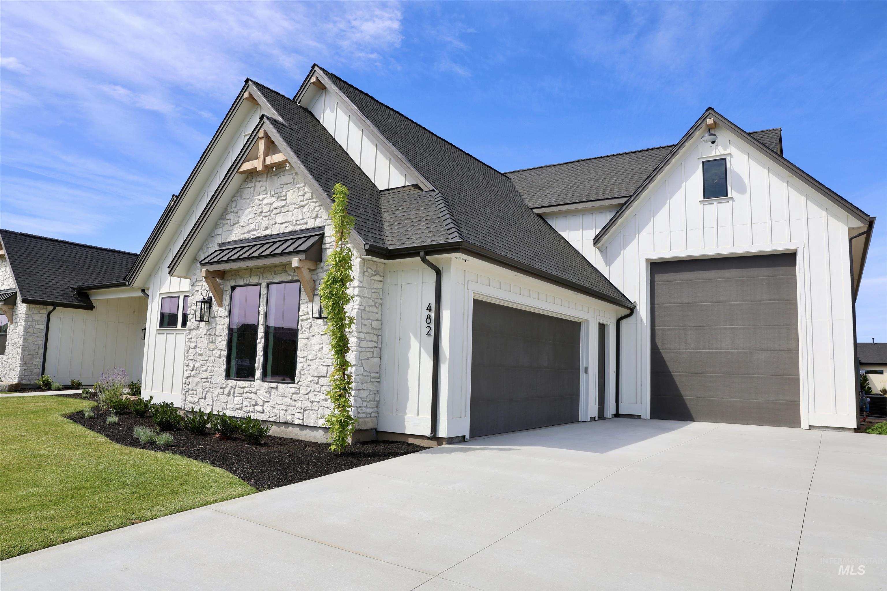 Modern farmhouse style home featuring board and batten siding, stone siding, a shingled roof, and concrete driveway