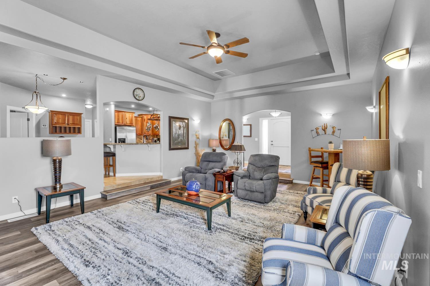 Living area with arched walkways, a ceiling fan, dark wood finished floors, and a raised ceiling