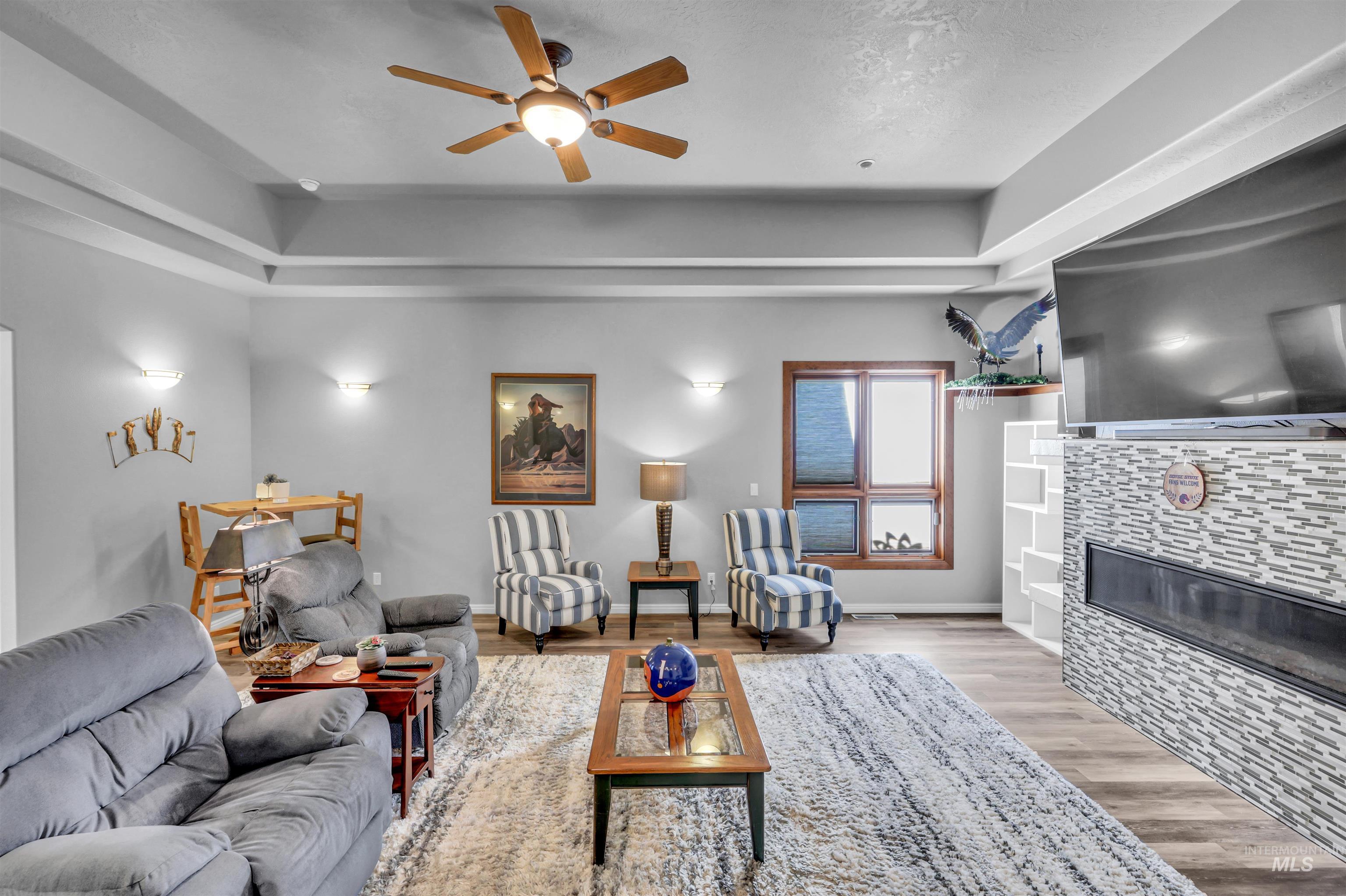 Living room with a tile fireplace, a ceiling fan, and light wood-style flooring