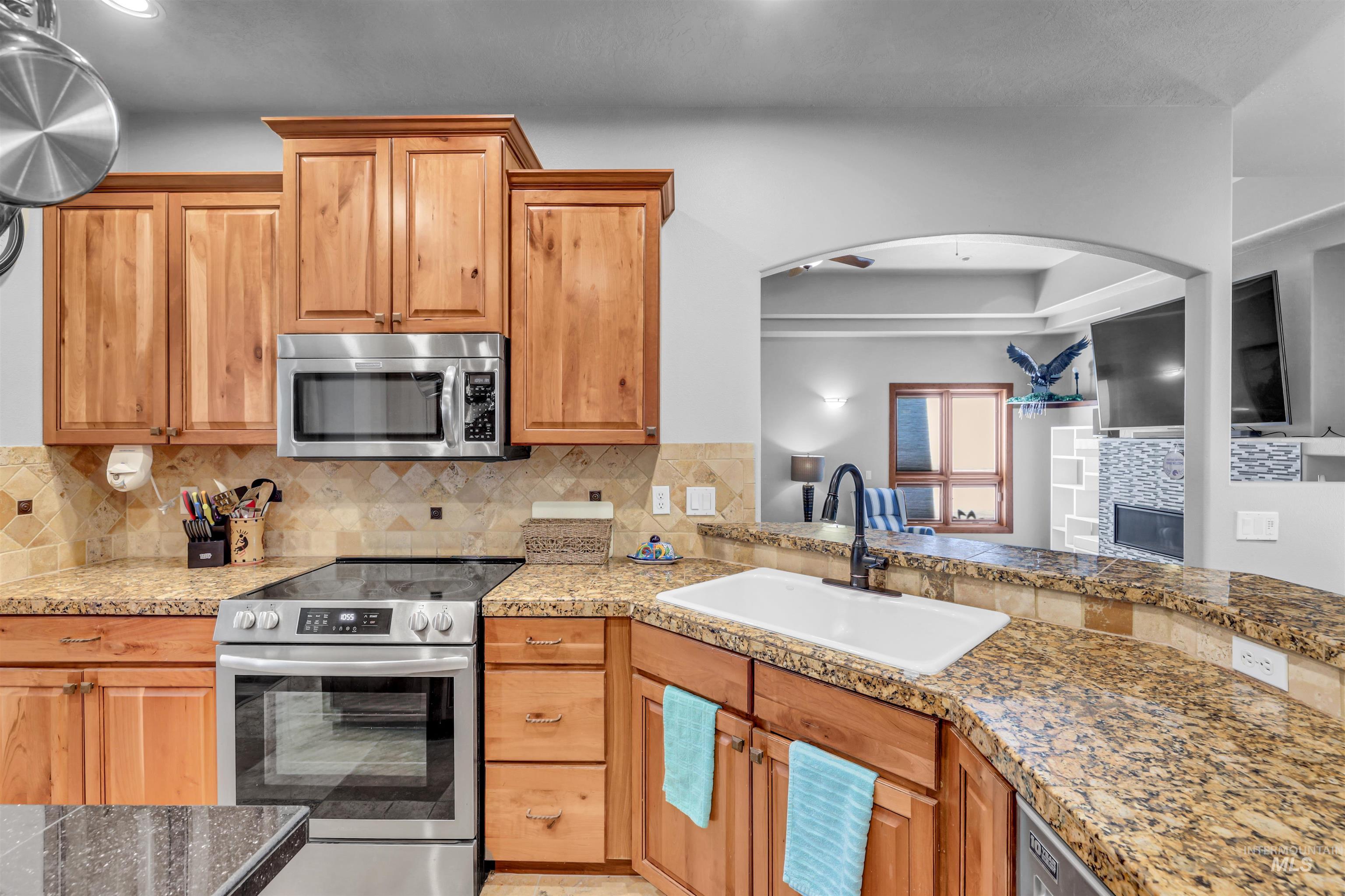 Kitchen with appliances with stainless steel finishes, decorative backsplash, a glass covered fireplace, and tile countertops