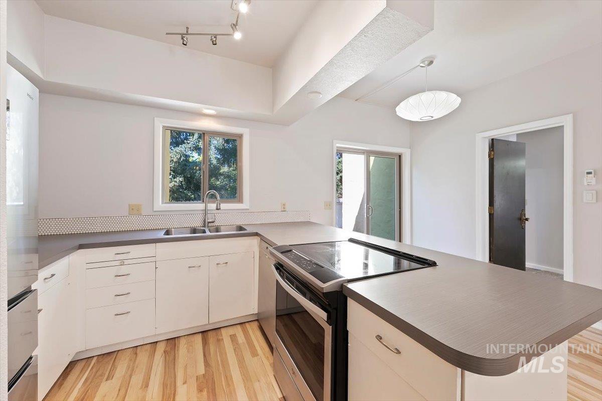 Kitchen featuring appliances with stainless steel finishes, light wood-type flooring, a peninsula, hanging light fixtures, and white cabinetry