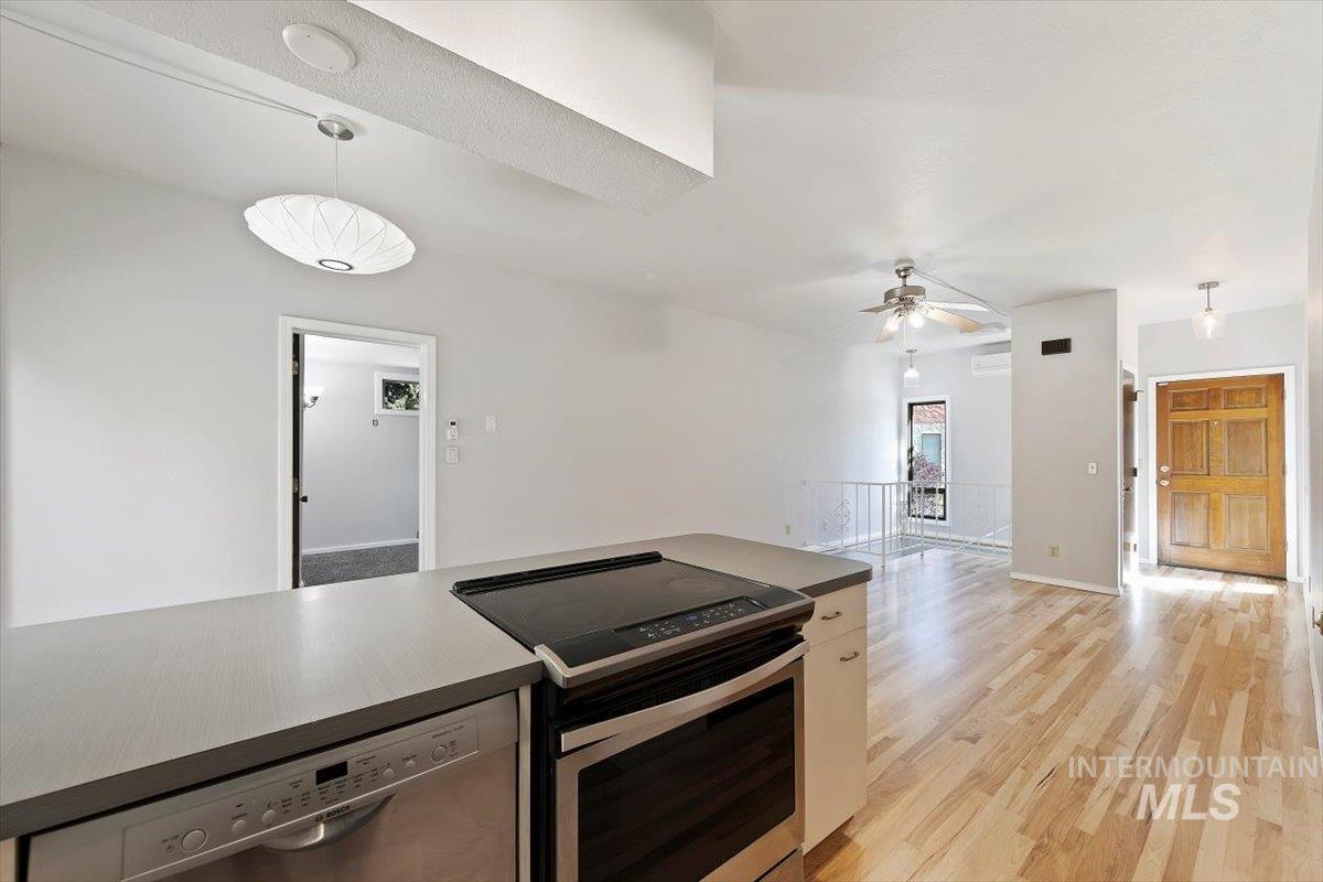 Kitchen with decorative light fixtures, appliances with stainless steel finishes, light wood-type flooring, ceiling fan, and open floor plan