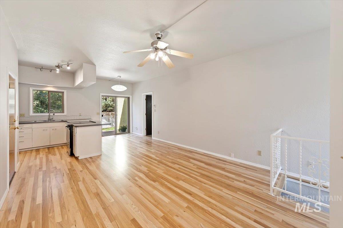 Kitchen featuring open floor plan, dark countertops, light wood-style floors, white cabinetry, and a ceiling fan