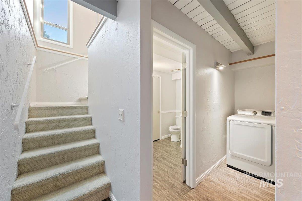 Stairway featuring washer / dryer, wood finished floors, a textured wall, and beam ceiling