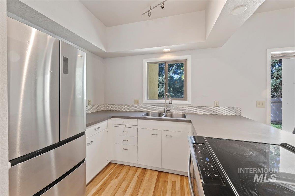 Kitchen featuring freestanding refrigerator, black range with electric cooktop, light wood-style flooring, white cabinets, and light countertops