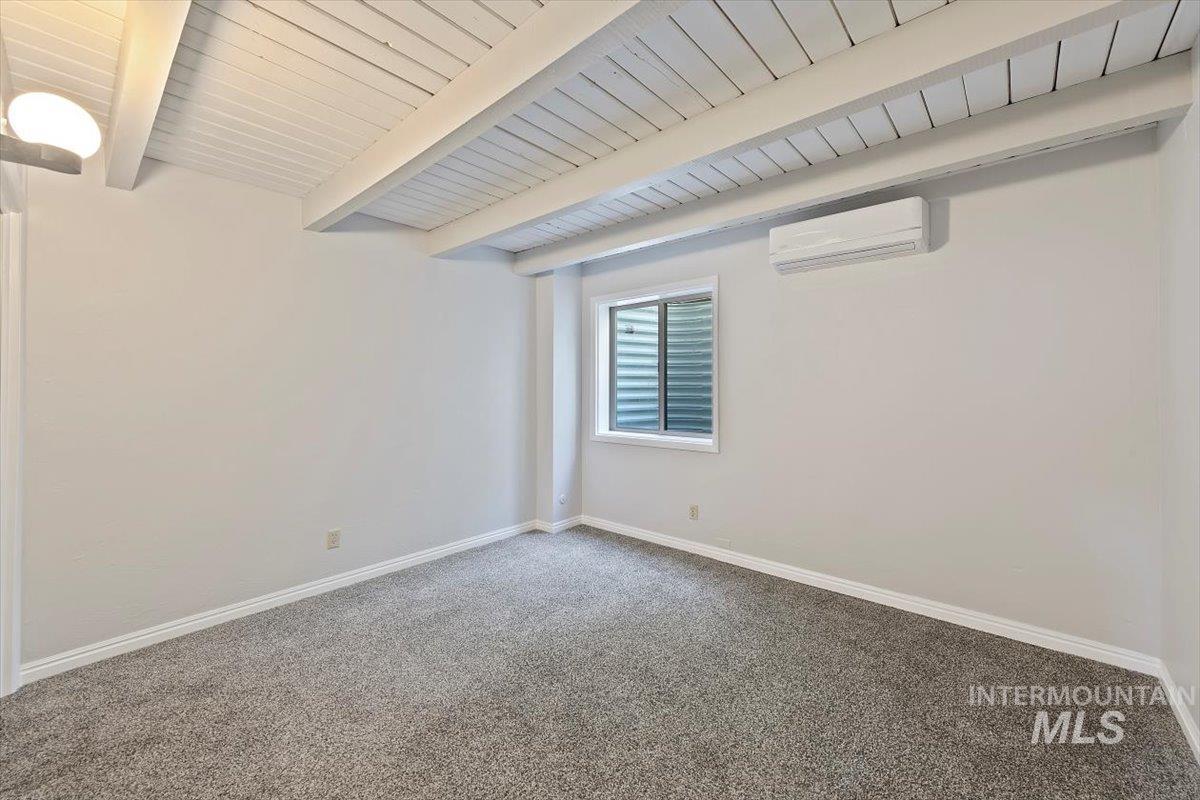Spare room featuring beam ceiling, carpet, and a wall unit AC