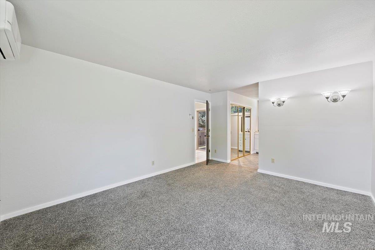Carpeted spare room with baseboards and a wall unit AC