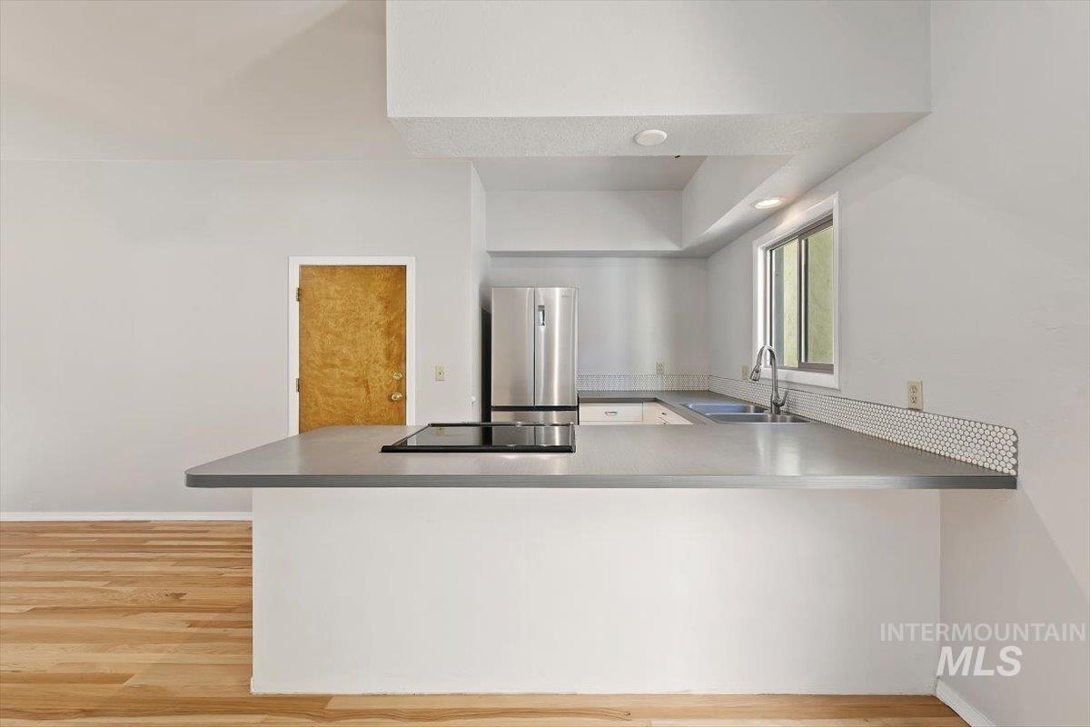Kitchen with a peninsula, freestanding refrigerator, light wood-style floors, black electric stovetop, and recessed lighting