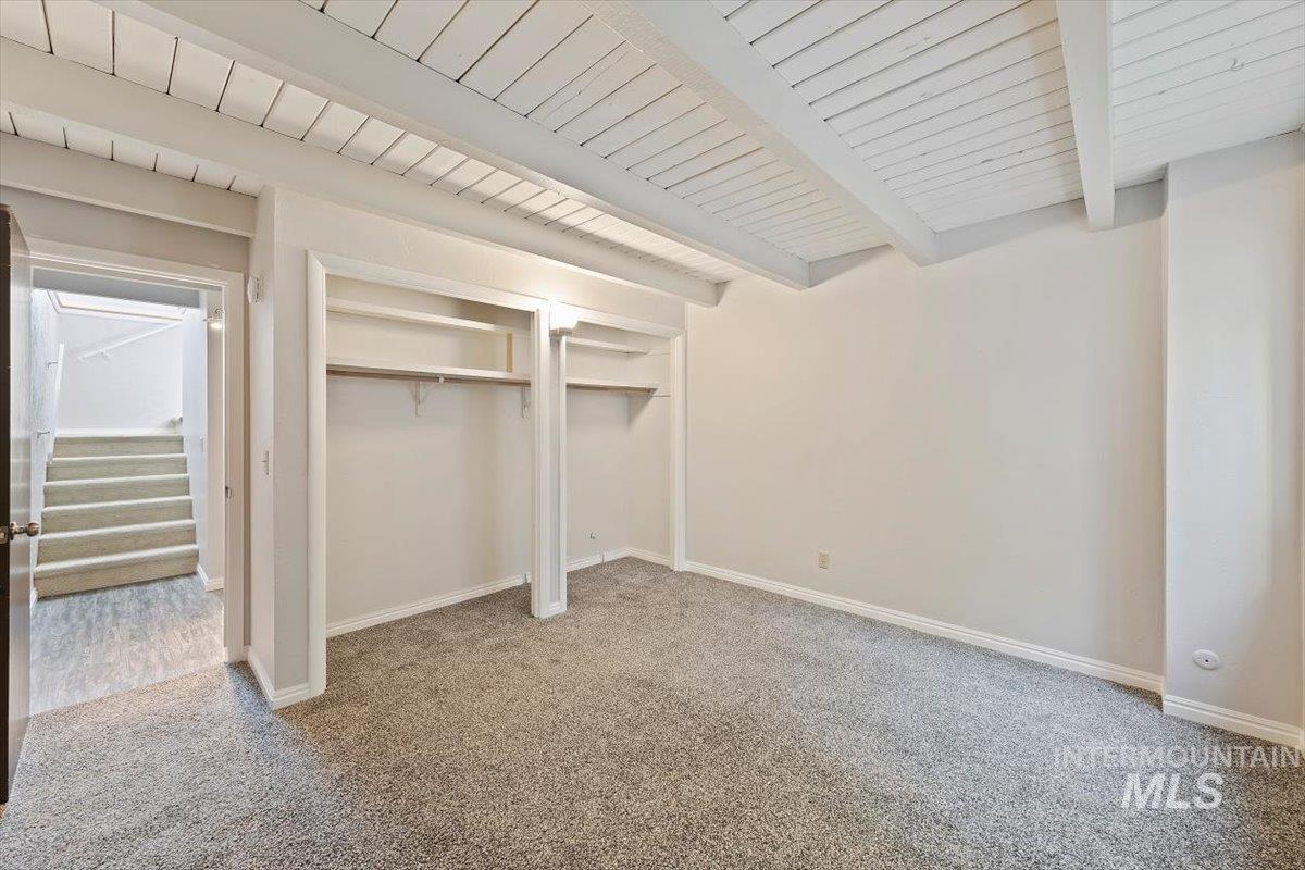 Unfurnished bedroom with a closet, light colored carpet, and beam ceiling