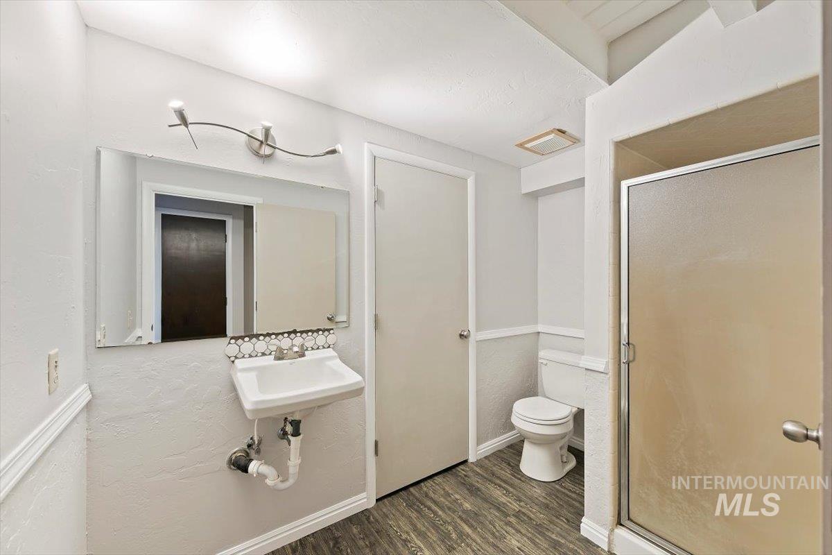 Bathroom featuring a shower stall, a textured wall, and dark wood-style floors